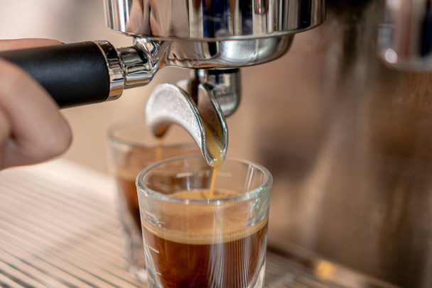 Macchina da caffè grigia con due tazzine di vetro riempite di caffè su una griglia metallica in primo piano. - Foto, immagini