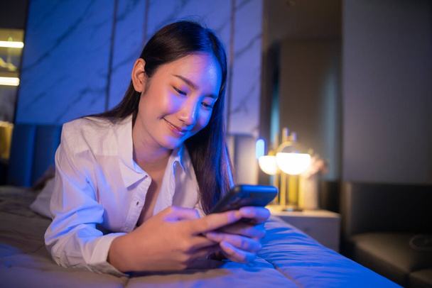 Young Asian beautiful woman enjoy using smartphone- tablet  enjoy  social online and facetime and listening music on bed with happy and smile in bedroom at night time. - Фото, зображення