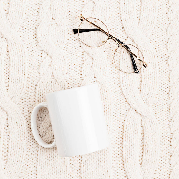 Mockup s bílým hrnkem a brýlemi na bílém vlněném pleteném pozadí. Útulná koncepce čtení. Byt ležel, horní pohled - Fotografie, Obrázek