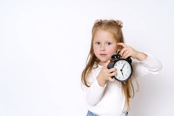 Children concept. A girl holds an alarm clock in her hands, plays with it, looks at the camera. Isolated over white background. - Фото, зображення
