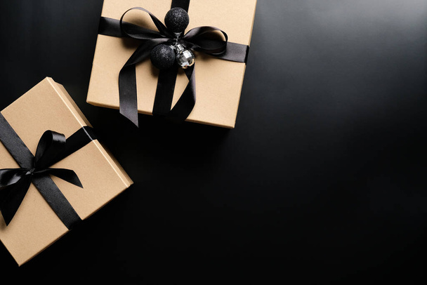 Κομψά Χριστουγεννιάτικα κουτιά δώρου με κορδέλα φιόγκο και μπάλες σε μαύρο φόντο. Επίπεδη θέα. Χριστούγεννα ή Μαύρη Παρασκευή έννοια πώληση - Φωτογραφία, εικόνα