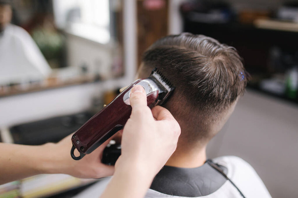 美容室で男性のバックビュー。理髪店で男性の散髪。新しいヘアカットスタイル2021 。プロの美容師は、髪をフリンジ用のヘアクリップを使用しています - 写真・画像