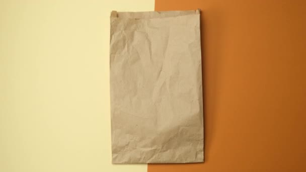 twee handen met een papieren zak bruin kraftpapier op een bruine achtergrond, bovenaanzicht - Video