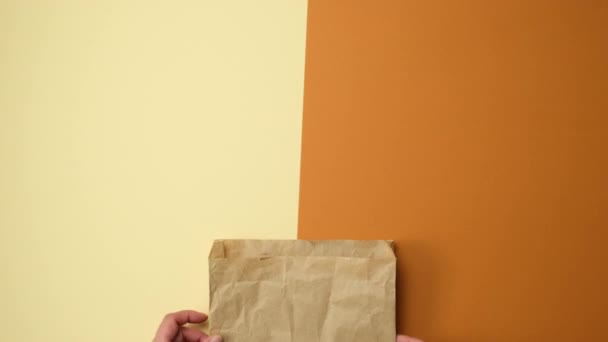 dos manos sosteniendo una bolsa de papel de kraft marrón sobre un fondo marrón, vista superior - Metraje, vídeo