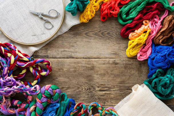 Frame of accessories for embroidery. Hoop, colorful floss threads and canvas on old wooden background, copyspace - Fotoğraf, Görsel