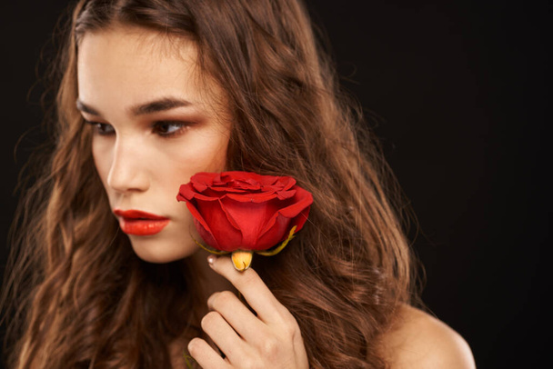γυναίκα με ένα κόκκινο τριαντάφυλλο σε σκούρο φόντο μακριά μαλλιά μακιγιάζ κόκκινα χείλη - Φωτογραφία, εικόνα