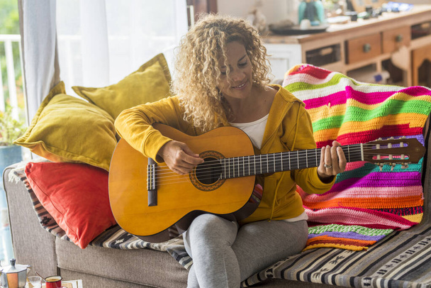 Красива жінка середнього віку грає на гітарі вдома - музичний урок і співачка сидить на дивані
 - Фото, зображення