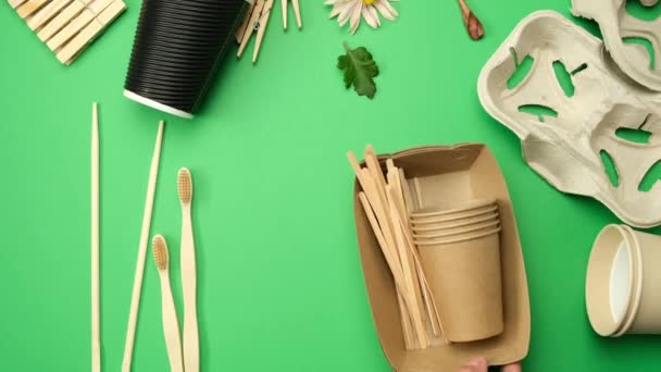 divers articles en matériau recyclable, gobelets en papier jetables et fourchettes en bois sur un fond vert, vue de dessus. Zéro déchet - Séquence, vidéo