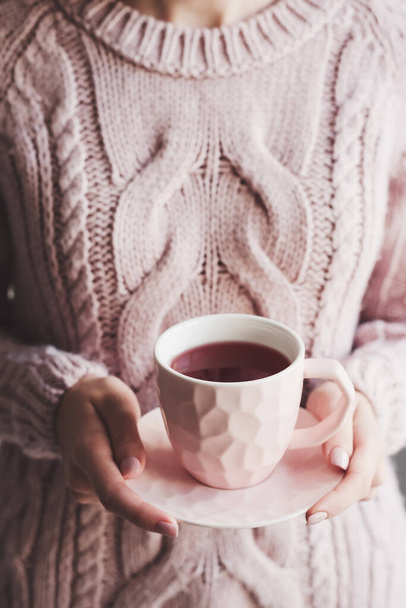 Γυναίκα σε ζεστό πλεκτό πουλόβερ κρατώντας ένα φλιτζάνι τσάι Hibiscus. Κόκκινο τσάι. Ζεστό φυτικό ποτό  - Φωτογραφία, εικόνα