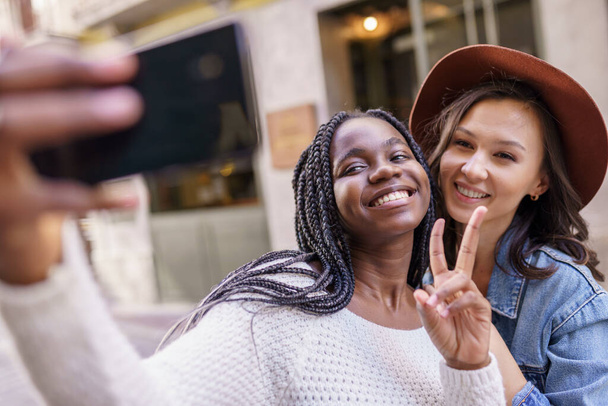 Two beautiful multiethnic women making selfie and grimacing - Photo, Image