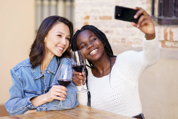 Дві жінки роблять селфі зі смартфоном, маючи келих вина
. - Фото, зображення