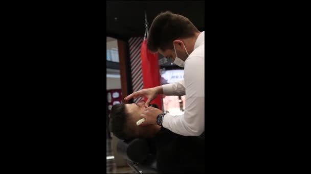 Vidéo verticale d'un coiffeur coupant la barbe du client - Séquence, vidéo