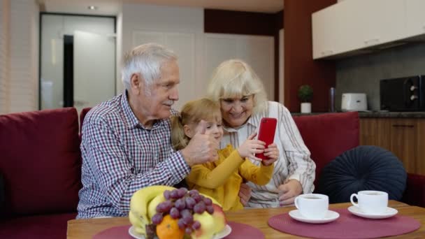 Старшая белая пара с симпатичной девочкой внучка с помощью мобильного телефона, смотреть смешные видео - Кадры, видео