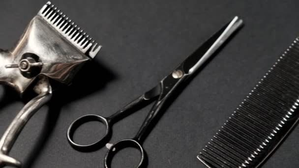 Auf einer schwarzen Oberfläche befinden sich alte Friseurwerkzeuge. Vintage manuelle Haarschneidemaschine, Kamm, Rasierer, Friseurschere. schwarz monochrom. Nahaufnahme. Barbershop-Hintergrund. Kontrastschatten. Schiebereglerbewegung. 4k. - Filmmaterial, Video
