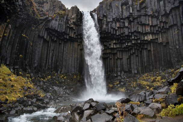 Voda padá přes čedičové sloupy u vodopádu Svartifoss v Národním parku Skaftafell na Islandu - Fotografie, Obrázek