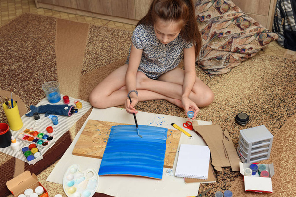 girl draws at home, artistic creation, makes creative artwork from paper, paints and brushes - Photo, Image