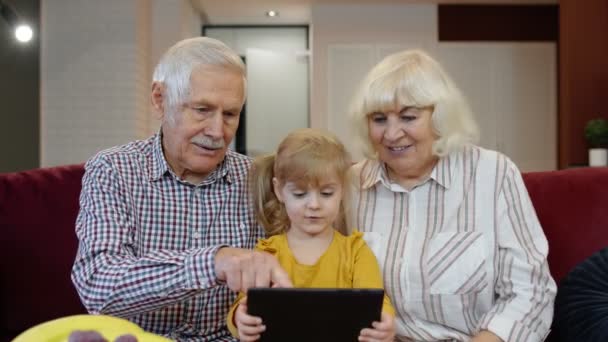 Lapsi tyttö näyttää jotain kannettavan isovanhemmille, eläkeläiset pari oppii käyttämään tablettia - Materiaali, video
