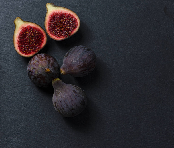 Still life of black figs. Three whole figs and one split fig. Dark Food. - Photo, Image