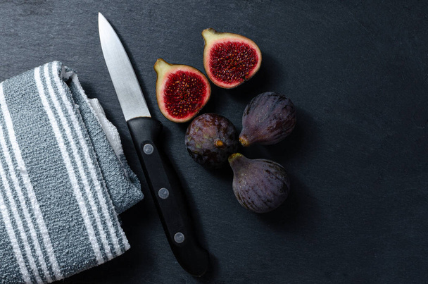 Still life of black figs with a knife and a cloth on a slate base. Three whole figs and one split. - Foto, afbeelding