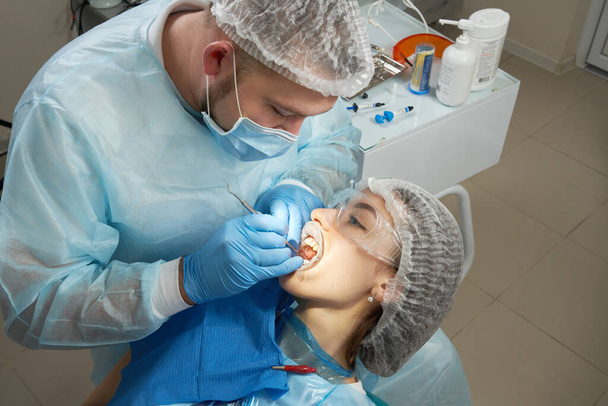 Οδοντίατρος κάνει οδοντιατρική θεραπεία σε μια γυναίκα ασθενή. Οδοντίατρος που εξετάζει τα δόντια ενός ασθενούς στο γραφείο σύγχρονης οδοντιατρικής - Φωτογραφία, εικόνα