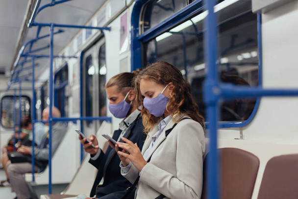 passengers wearing protective masks using their smartphones while sitting in a subway car. - Valokuva, kuva