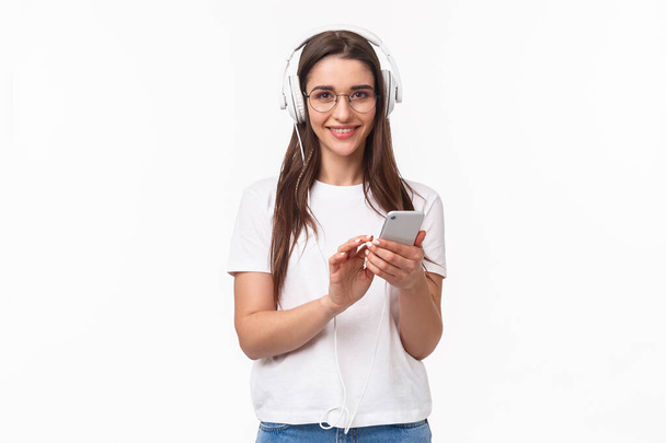 Tecnologia, estilo de vida e conceito de música. Retrato de carismático, sorrindo jovem mulher em fones de ouvido, ouvindo músicas playlist, comprou conta premium, desfrutando de podcast favorito, fundo branco - Foto, Imagem