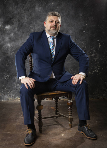 Mature businessman in a suit sitting on chair studio portrait. - Zdjęcie, obraz