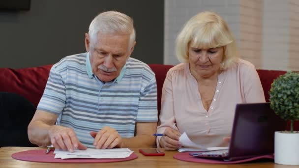 Senior pensioner couple checking and calculating domestic bills bank loan payment doing paperwork - Imágenes, Vídeo
