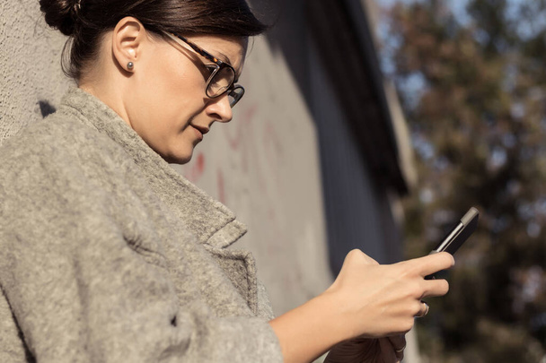 Mujer escribiendo mensaje de texto en el teléfono celular al aire libre. Empresaria usando teléfono móvil en la ciudad. - Foto, imagen