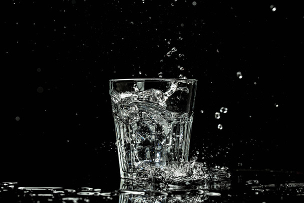 Spatten en druppels water in een glas worden geïsoleerd op een zwarte achtergrond. plaats voor tekst. - Foto, afbeelding
