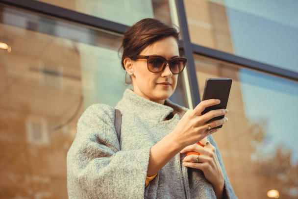 Belle femme tapant message texte sur téléphone intelligent sur sa pause café à l'extérieur. Focus est à portée de main et téléphone.  - Photo, image