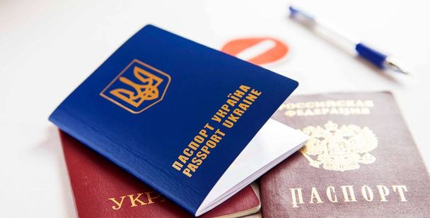 Oekraïense en Russische paspoort close-up, verbod en pen op de achtergrond - Foto, afbeelding