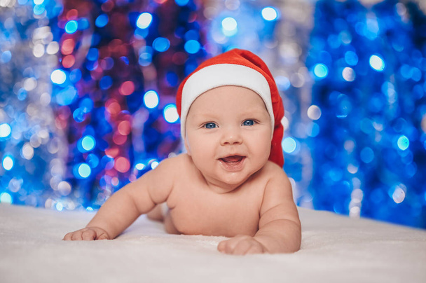 Baby first Christmas. Child in Santa hat. Cute emotional smiling funny newborn facial expressions. - Foto, Imagen