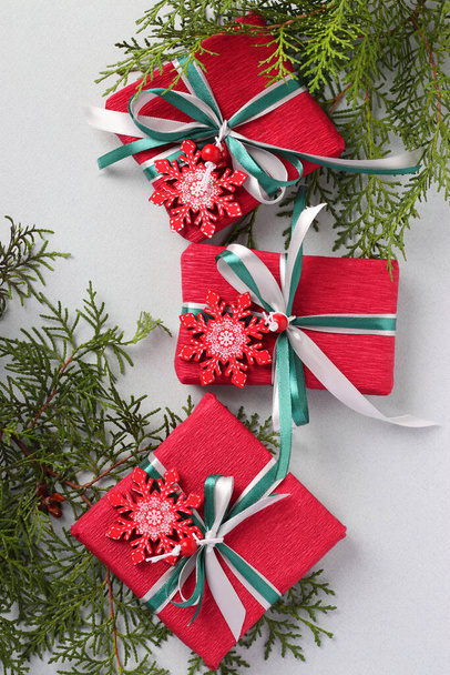 Három karácsonyi ajándék piros papíron hópelyhekkel és szalagokkal a világos felületen. Karácsonyi ajándékok. Üdülési kártya. Függőleges formátum - Fotó, kép