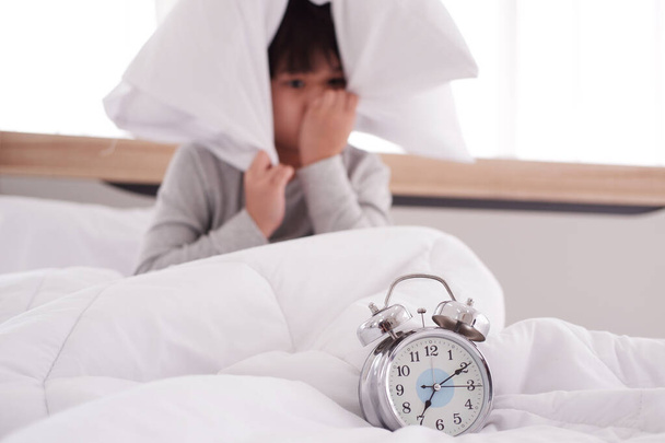 Asian Boy wordt laat wakker op 07: 00 en lui om naar school te gaan. Gesloten en focus op klok op wit bed in de slaapkamer. - Foto, afbeelding