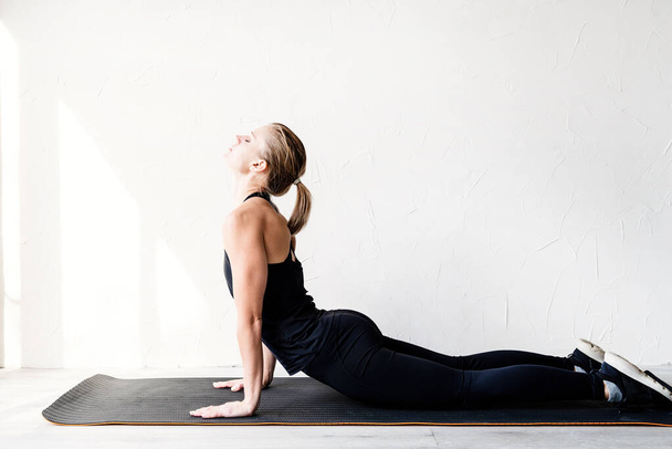 Healthy lifestyle. Sport and fitness. Young blond woman doing yoga or stretching at home - 写真・画像
