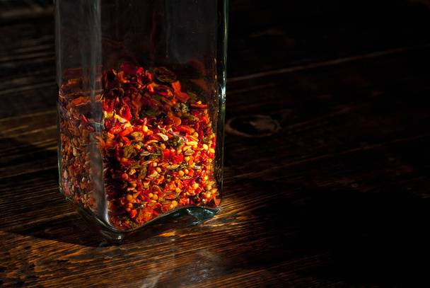 A mixture of various spices in a glass jar close up. Spices on a black, old shabby board. Free space and copy space for text near condiments. Contrasting dramatic light as an artistic effect. - Foto, Imagem