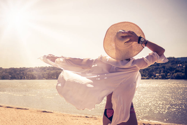 Vista trasera de mujer despreocupada con sombrero de paja disfrutando de la brisa de verano en la playa. Copiar espacio.  - Foto, imagen
