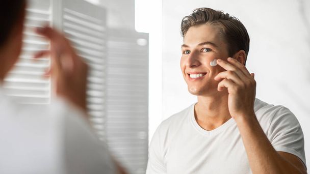 Handsome guy looking in the mirror applying cream - Photo, Image