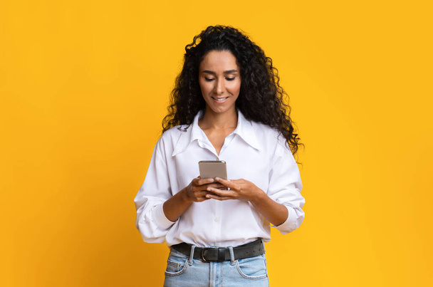 Stylish Brunette Woman Using Smartphone Over Yellow Background In Studio - Photo, Image