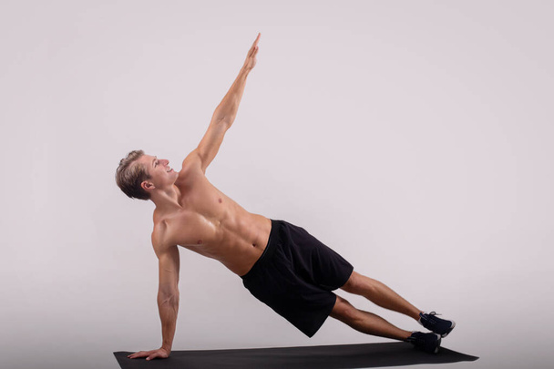 Full length portrait of athletic young guy doing side plank over light studio background, copy space - Фото, изображение