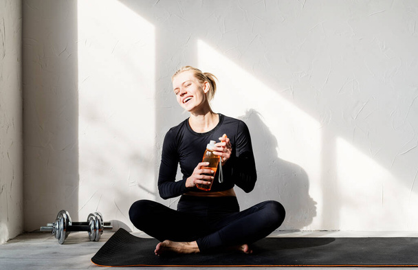 Healthy lifestyle. Sport and fitness. Young blond woman doing yoga or meditating at home drinking water - Foto, Imagen