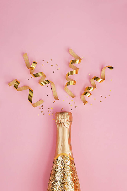 Gold glittering bottle of champagne and swirls on pink background - Photo, image