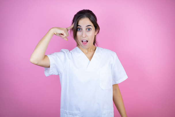 Young brunette doctor girl wearing nurse or surgeon uniform over isolated pink background smiling and thinking with her fingers on her head that she has an idea. - Photo, Image
