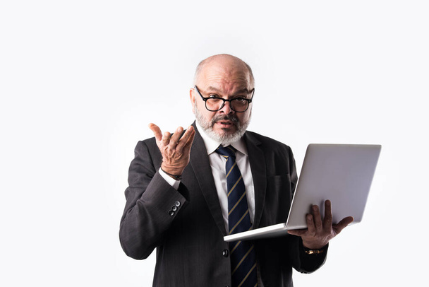 Портрет старшого індійського бізнесмена, який користується ноутбуком, планшетом або смартфоном, стоячи навпроти білого фону, демонструючи або представляючи - Фото, зображення