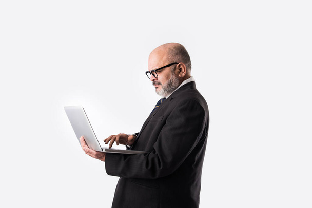 Portrait of Senior Indian asian businessman using laptop, tablet or smartphone while standing against white background, showing or presenting - Foto, Imagem