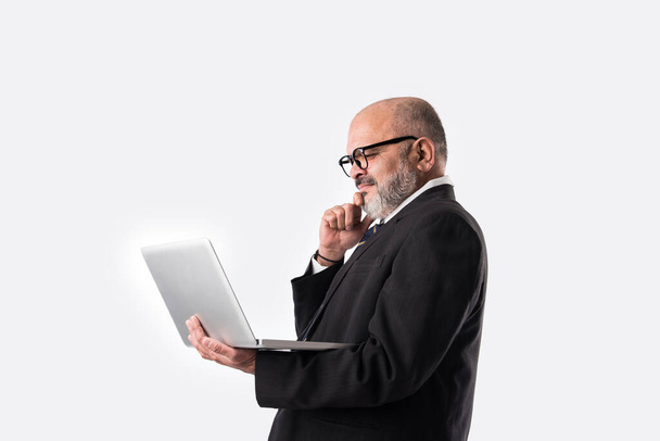 Portrait of Senior Indian asian businessman using laptop, tablet or smartphone while standing against white background, showing or presenting - Foto, imagen