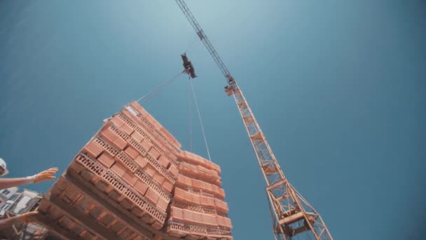 Arbeiter steckten von einem Kran angehobene rote Ziegelsteine fest - Filmmaterial, Video