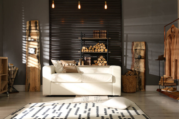 Shelving unit with stacked firewood and comfortable sofa in stylish room interior - Zdjęcie, obraz