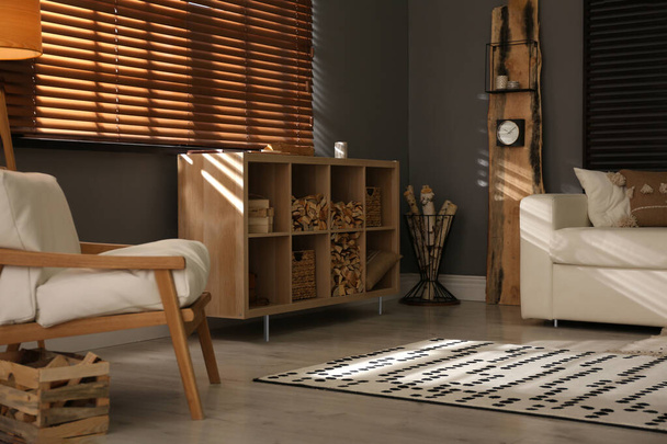 Shelving unit with stacked firewood and comfortable sofa in stylish room interior - Foto, Imagem